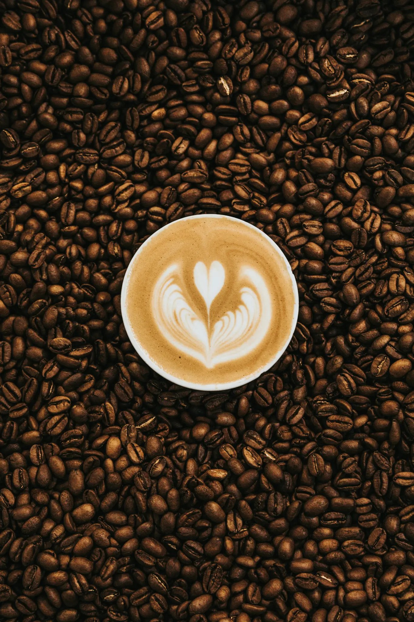 Latte art heart in a cup surrounded by coffee beans