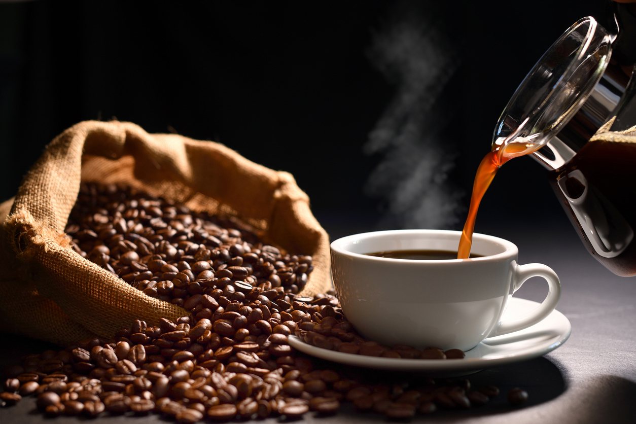 Rich coffee being poured into a white cup with coffee beans